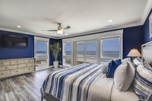 A bedroom with a large bed, a ceiling fan, a potted plant, and a view of the ocean through large windows. - Lazy Daze: Oceanfront, Endless Coastal Views & Pool (Murrells Inlet)