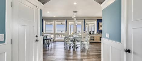 A hallway with a wooden floor, white doors, and a view of the ocean through large windows.