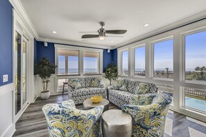 A sunroom with large windows, a ceiling fan, and patterned furniture. - Lazy Daze: Oceanfront, Endless Coastal Views & Pool (Murrells Inlet)