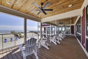 A covered outdoor deck with Adirondack chairs, a ceiling fan, and a view of the beach. - Lazy Daze: Oceanfront, Endless Coastal Views & Pool (Murrells Inlet)