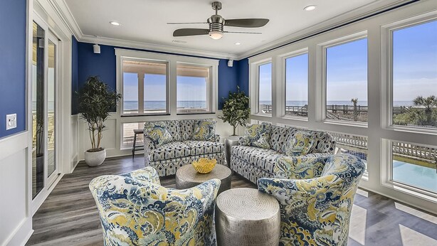 A sunroom with large windows, a ceiling fan, and patterned furniture. - Lazy Daze: Oceanfront, Endless Coastal Views & Pool (Murrells Inlet)