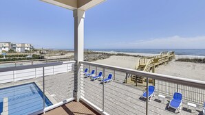A balcony with a pool, beach chairs, and a view of the beach and ocean. - Lazy Daze: Oceanfront, Endless Coastal Views & Pool (Murrells Inlet)