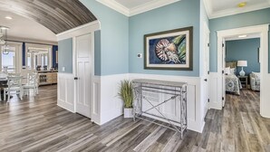 A spacious living area with a high ceiling, a dining area with a view, and a hallway leading to another room. - Lazy Daze: Oceanfront, Endless Coastal Views & Pool (Murrells Inlet)