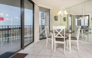 Ein Essbereich mit einem runden Tisch und weißen Stühlen, ein Balkon mit Geländer und Blick auf den Strand.