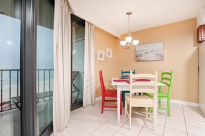 Ein Balkon mit Glastür, einem Esstisch mit Stühlen, einer Deckenleuchte und einem Gemälde an der Wand.