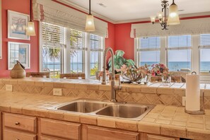 A kitchen with a double sink, wooden cabinets, and a view of the ocean through large windows. - Majestic Dream: Oceanfront, Pool, Hot Tub & Endless Coastal Days (Murrells Inlet)