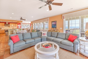A spacious living area with a gray sectional sofa, a round glass coffee table, and a ceiling fan. - Majestic Dream: Oceanfront, Pool, Hot Tub & Endless Coastal Days (Murrells Inlet)