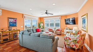 A living room with a sectional sofa, a TV, and a view of the outdoors. - Majestic Dream: Oceanfront, Pool, Hot Tub & Endless Coastal Days (Murrells Inlet)