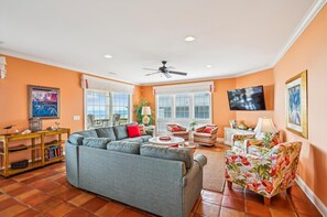 A living room with a sectional sofa, a TV, and a view of the outdoors. - Majestic Dream: Oceanfront, Pool, Hot Tub & Endless Coastal Days (Murrells Inlet)