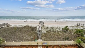 A beach view with a wooden boardwalk leading to the ocean, a white picket fence, and a warning sign. - Majestic Dream: Oceanfront, Pool, Hot Tub & Endless Coastal Days (Murrells Inlet)