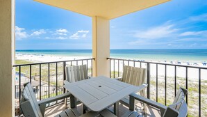 A balcony with a table and chairs overlooking a beach with a clear sky. - Phoenix Iii 3047 1 Bedroom Condo (Orange Beach)