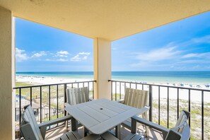 Ein Balkon mit Tisch und Stühlen mit Blick auf einen Strand und einen klaren Himmel.