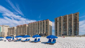 A beachfront hotel with multiple high-rise buildings, beach umbrellas, and sun loungers. - Phoenix Iii 3047 1 Bedroom Condo (Orange Beach)