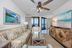 Ein Hotelzimmer mit einer Couch, einem Sessel, einem Couchtisch, einem Fernseher und einem Deckenventilator.