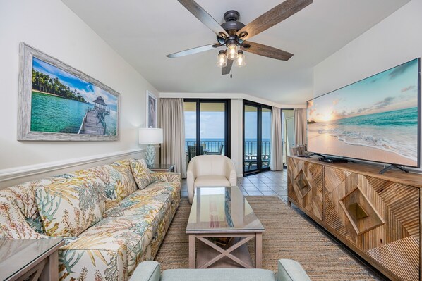 A hotel room with a sofa, a chair, a coffee table, a TV, and a ceiling fan. - Phoenix Iii 3047 1 Bedroom Condo (Orange Beach)