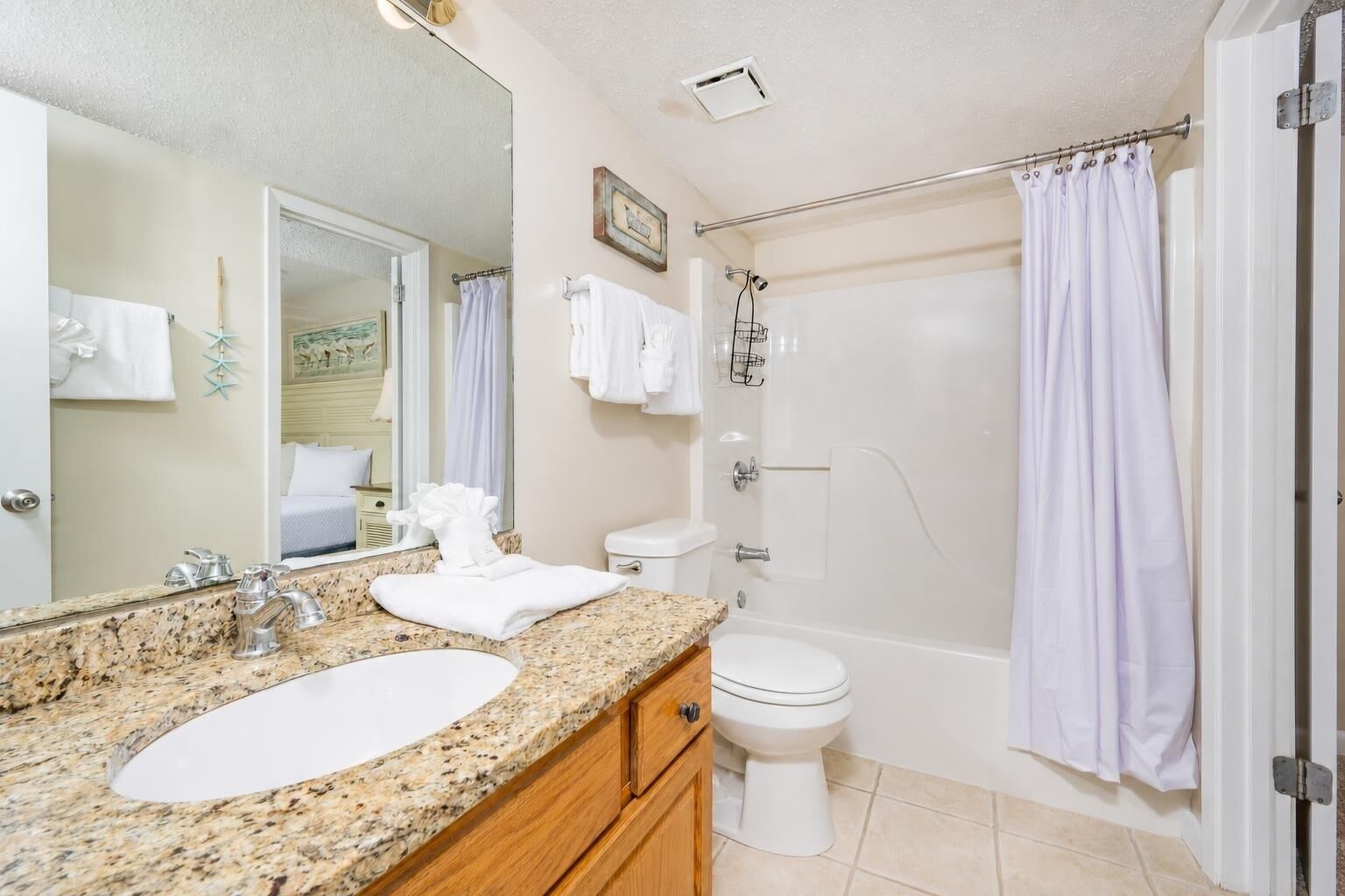 A bathroom with a granite countertop, two sinks, a toilet, a shower with a curtain, and a mirror.
