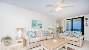 A living room with two beige sofas, a wooden coffee table, a ceiling fan, and a large window with a view. - Phoenix Vii 7602 1 Bedroom Condo (Orange Beach)