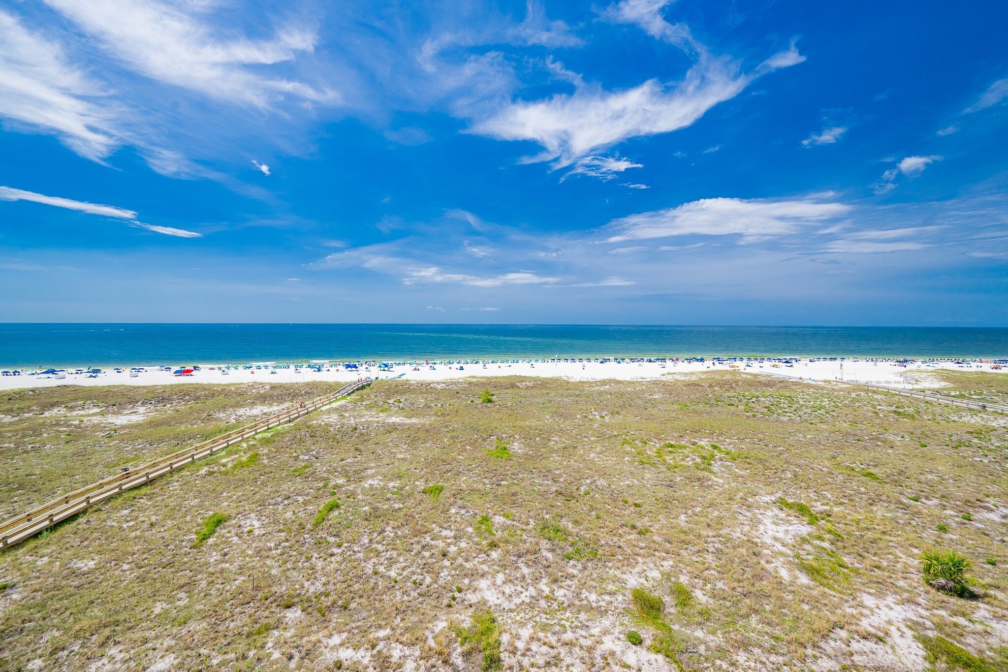 A beach with a clear sky, a sandy shore, and a grassy area with a wooden pathway.