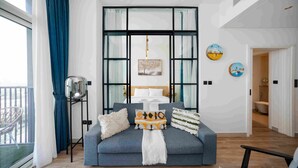 A modern living room with a sofa, cushions, a hanging light fixture, and artwork on the wall. - Boho-chic 1BR w Pool Dubai Hills (Dubai)