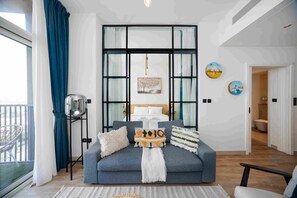 A modern living room with a sofa, cushions, a hanging light fixture, and artwork on the wall. - Boho-chic 1BR w Pool Dubai Hills (Dubai)