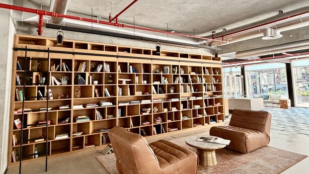 A modern library with a large bookshelf, leather armchairs, and a coffee table. - Boho-chic 1BR w Pool Dubai Hills (Dubai)
