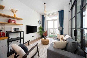 A modern living room with a sofa, a TV, a coffee machine, and a plant. - Boho-chic 1BR w Pool Dubai Hills (Dubai)