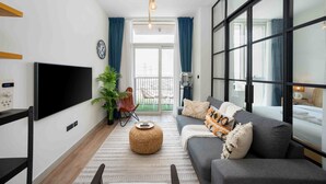 A modern living room with a flat-screen TV, a sofa, a coffee table, and a large window. - Boho-chic 1BR w Pool Dubai Hills (Dubai)