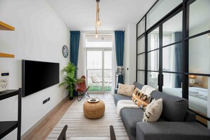 A modern living room with a flat-screen TV, a sofa, a coffee table, and a large window. - Boho-chic 1BR w Pool Dubai Hills (Dubai)