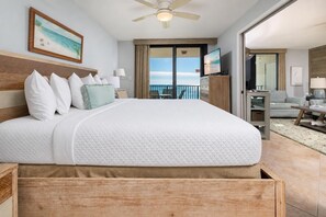 A hotel room with a large bed, a ceiling fan, a TV, a balcony with a view, and a seating area with a table and chairs. - Phoenix Vii 7804 2 Bedroom Condo (Orange Beach)