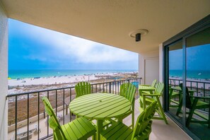 Un balcon avec une table et des chaises, donnant sur une plage parsemée de parasols et sur une jetée.
