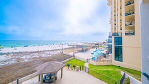 A balcony with a view of a beach, a pool area, and a building with multiple balconies. - Phoenix Iii 3022 1 Bedroom Condo (Orange Beach)