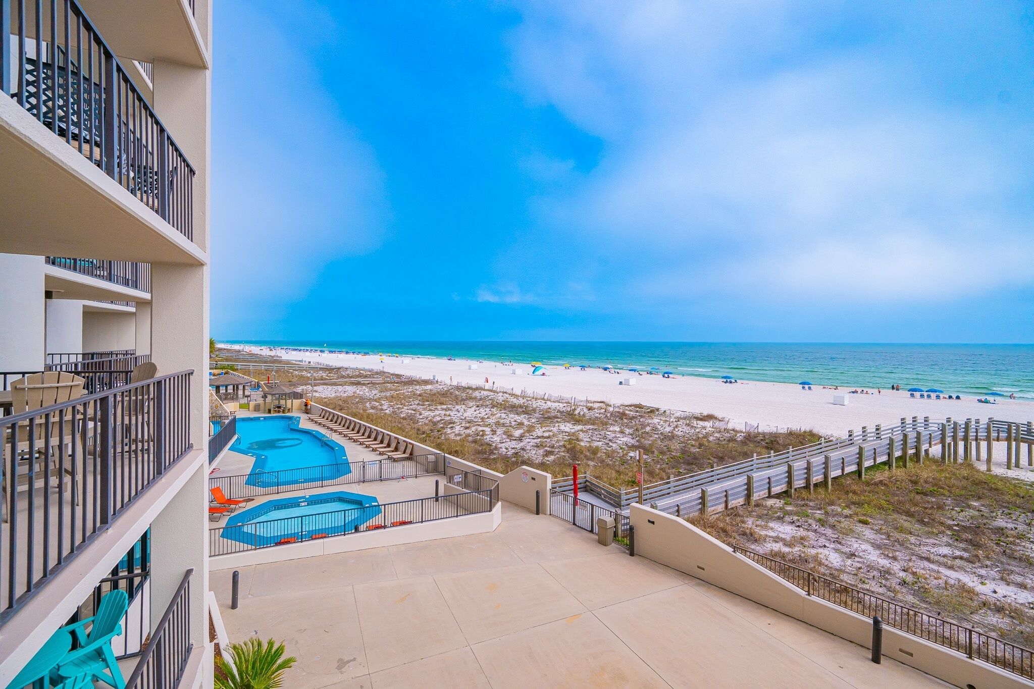 A hotel balcony with a view of a beach, a pool area, and a sandy beach.