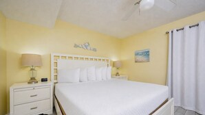 A hotel room with a bed, two bedside tables with lamps, a ceiling fan, a painting on the wall, and a window with curtains. - Phoenix Iii 3022 1 Bedroom Condo (Orange Beach)
