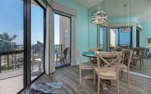 A modern dining area with wooden chairs and a table, large windows, and a view of the outdoors. - Phoenix Vii 7114 1 Bedroom Condo (Orange Beach)