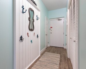 A hallway with a white door, a mirror, and wall-mounted hooks. - Phoenix Vii 7114 1 Bedroom Condo (Orange Beach)