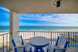 A balcony with a view of the ocean, a round table, and two Adirondack chairs. - Phoenix Iii 3072 1 Bedroom Condo (Orange Beach)