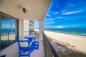 Ein Balkon mit Tisch und Stühlen, der Blick auf einen Strand und den Ozean gewährt.