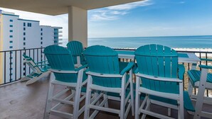 A balcony with teal Adirondack chairs, a view of the ocean, and a building in the background. - Phoenix Vii 7917 3 Bedroom Condo (Orange Beach)