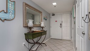 A hallway with a green console table, two white lamps, a large mirror, and a sign that reads 'MERMAIDS PLEASE ENTER'. - Phoenix Vii 7917 3 Bedroom Condo (Orange Beach)