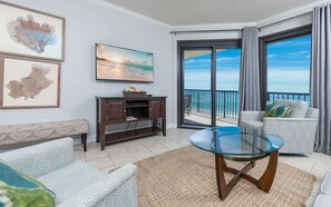 Un soggiorno con tavolo in vetro, divano, mobile TV e un balcone con vista sul mare.