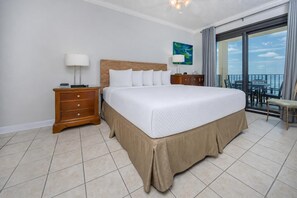 Ein Hotelzimmer mit einem großen Bett, einem Nachttisch aus Holz, einer Lampe, einem Gemälde und einem Balkon mit Blick.