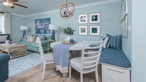Una sala de estar con una mesa de comedor redonda, sillas blancas, un sofá verde y una pared azul decorativa.