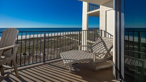 Un balcón con vista a la playa, dos sillas Adirondack y un ventanal.