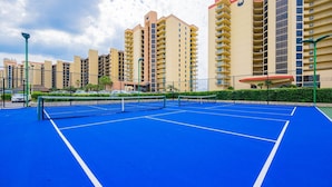 A tennis court with a net, surrounded by a fence, and adjacent to residential buildings. - Phoenix Iii 3075 1 Bedroom Condo (Orange Beach)