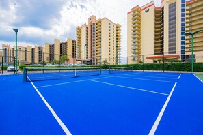 A tennis court with a net, surrounded by a fence, and adjacent to residential buildings. - Phoenix Iii 3075 1 Bedroom Condo (Orange Beach)