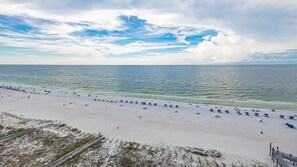 Ein Strand mit Reihen von Sonnenschirmen und Liegestühlen, eine sandige Küstenlinie und eine Straße parallel zum Strand.