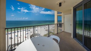 Un balcon donnant sur une plage, avec une table et deux chaises.