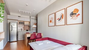 Et moderne hotelværelse med seng, skrivebord, stol, tekøkken og kunst på væggen.