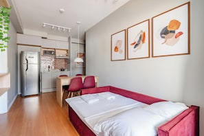 A modern hotel room with a bed, a desk, a chair, a kitchen area, and artwork on the wall. - Maison (São Paulo)