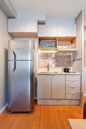 A compact kitchen with a stainless steel refrigerator, a microwave, and a sink. - Maison (São Paulo)